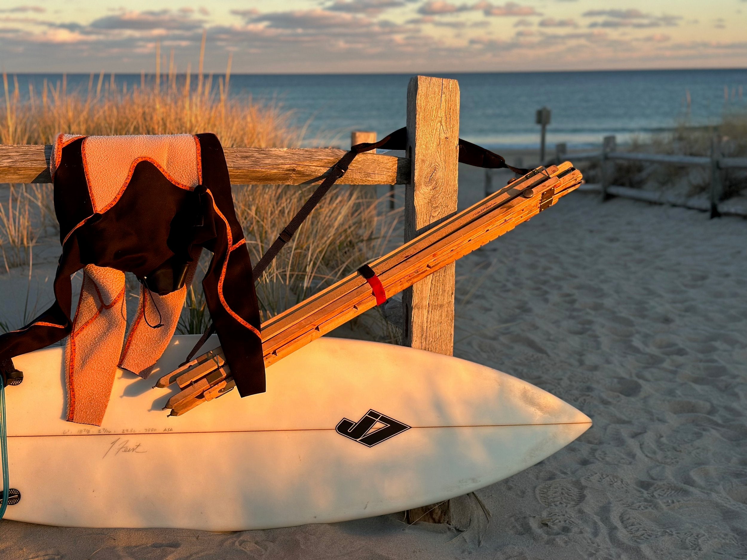 The Nadeau Easel hanging on a fence next to a surfboard and wetsuit.