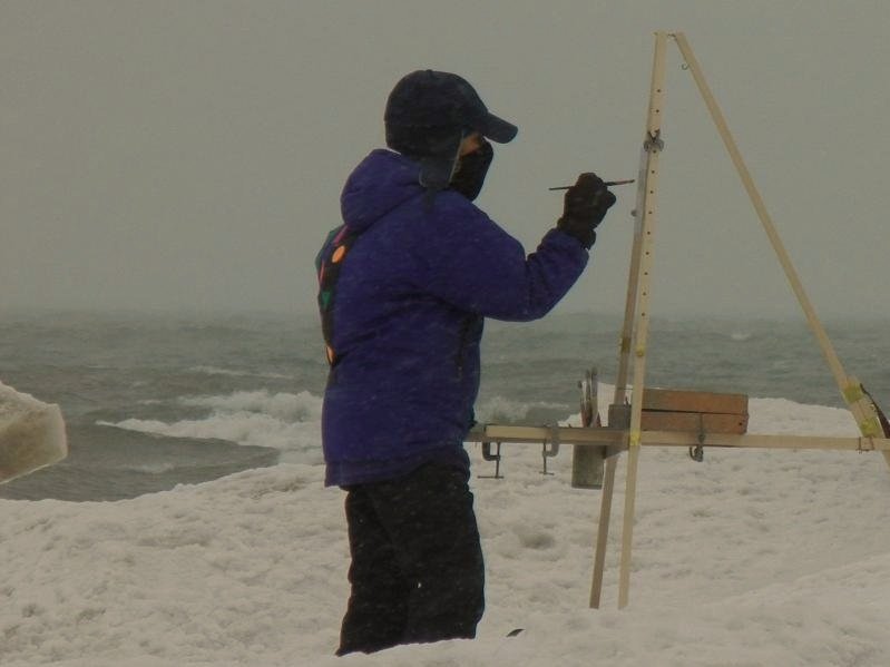Artist paining in winter gear on a snowy coastline with The Nadeau Easel.